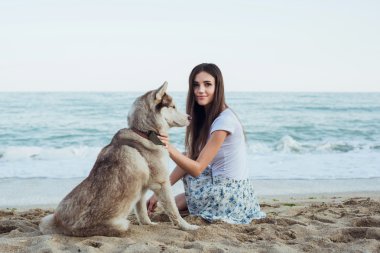 Genç beyaz kadın oynamak ve eğlenmek ile Sibirya husky köpek sahilde