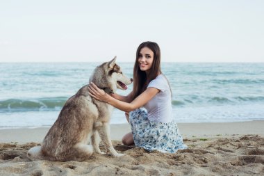 Genç beyaz kadın oynamak ve eğlenmek ile Sibirya husky köpek sahilde