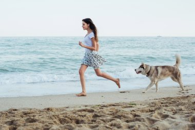 Genç beyaz kadın oynamak ve eğlenmek ile Sibirya husky köpek sahilde