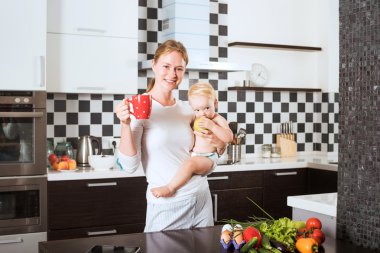 Anne Holding kızı taze sebze ve meyve yemek sırasında mutfak. Anne ve küçük kızı bir elma tutan mutfak üzerinde. Sağlıklı gıda ve sağlıklı yaşam kavramı
