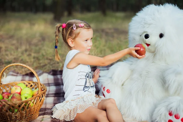 Niña divirtiéndose en el parque con juguete de oso y manzanas — Foto de Stock