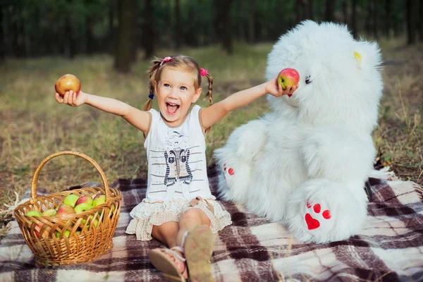 Menina se divertindo no parque com urso brinquedo e maçãs — Fotografia de Stock