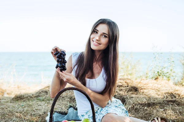 Junge kaukasische Hündin am Meer mit Korb mit Früchten. Mädchen essen Obst, gesunde Ernährung und gesundes Lebenskonzept — Stockfoto