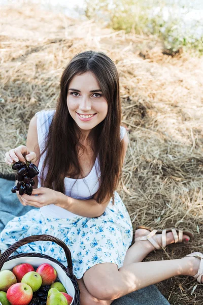 Hembra joven caucásica en la orilla del mar con canasta con frutas. Niña comiendo frutas, alimentación saludable y concepto de vida saludable — Foto de Stock