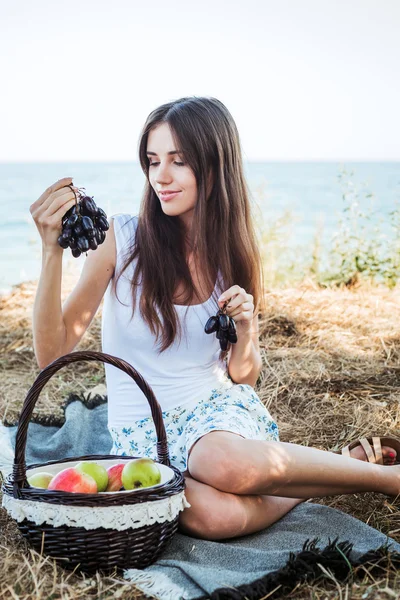 Junge kaukasische Hündin am Meer mit Korb mit Früchten. Mädchen essen Obst, gesunde Ernährung und gesundes Lebenskonzept — Stockfoto