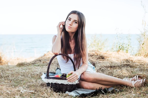 Fêmea caucasiana jovem à beira-mar com cesta com frutas. Menina comendo frutas, alimentação saudável e conceito de vida saudável — Fotografia de Stock