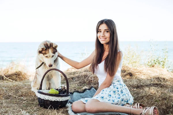 Young caucasian female and red siberian husky dog on seaside with basket with fruits. eating fruits, healthy eating and healthy living concept — Φωτογραφία Αρχείου