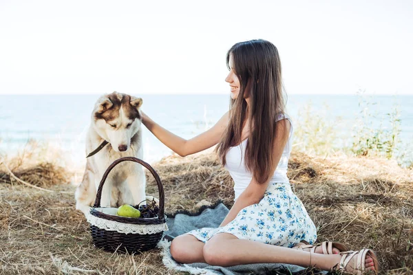 Young caucasian female and red siberian husky dog on seaside with basket with fruits. eating fruits, healthy eating and healthy living concept — Stockfoto