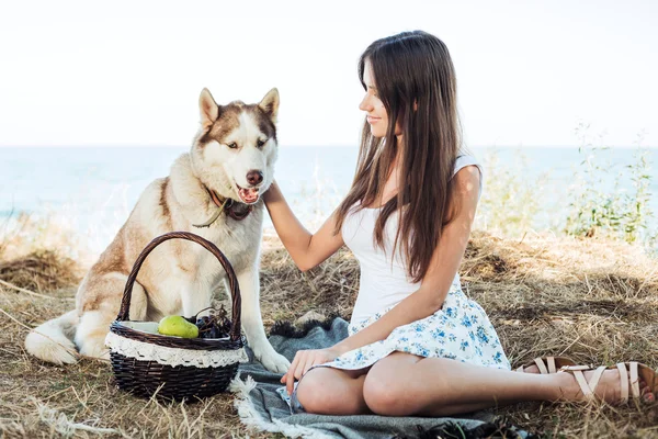 Joven hembra caucásica y perro husky siberiano rojo en la orilla del mar con canasta con frutas. comer frutas, alimentación saludable y concepto de vida saludable — Foto de Stock