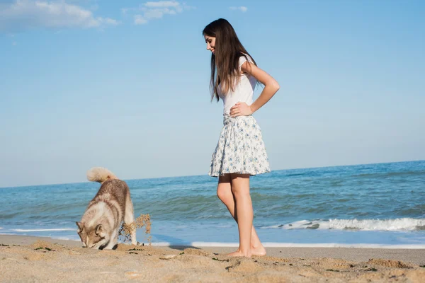 Unga kaukasiska kvinnliga spela och ha roligt med siberian husky hund på stranden — Stockfoto