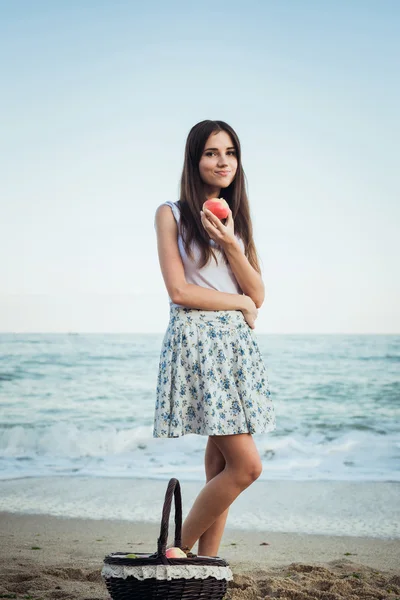 Jovem caucasiana fêmea com braquete com maçãs e frutas na praia. Conceito de vida saudável e alimentação saudável — Fotografia de Stock