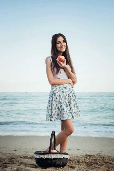 Jovem caucasiana fêmea com braquete com maçãs e frutas na praia. Conceito de vida saudável e alimentação saudável — Fotografia de Stock