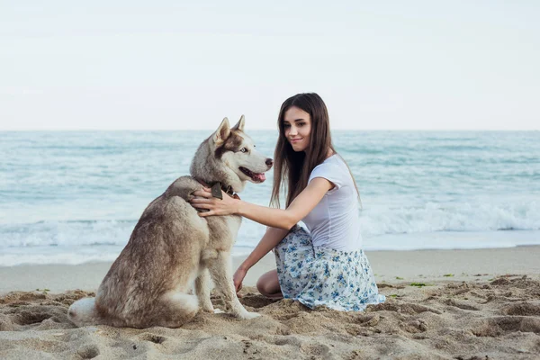 Młody kaukaski kobiece gry i zabawy z psem husky syberyjski na plaży — Zdjęcie stockowe