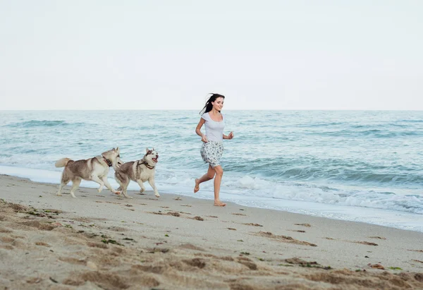 Junge kaukasische Hündin spielt und amüsiert sich mit sibirischem Husky-Hund am Strand — Stockfoto