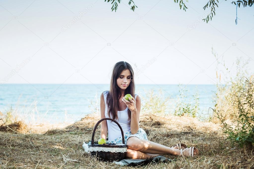 young caucasian female on seaside with basket with fruits. Girl eating fruits, healthy eating and healthy living concept