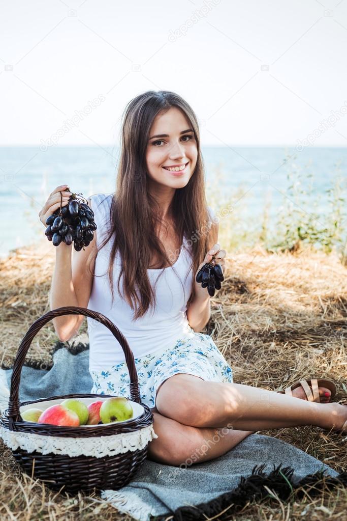 young caucasian female on seaside with basket with fruits. Girl eating fruits, healthy eating and healthy living concept