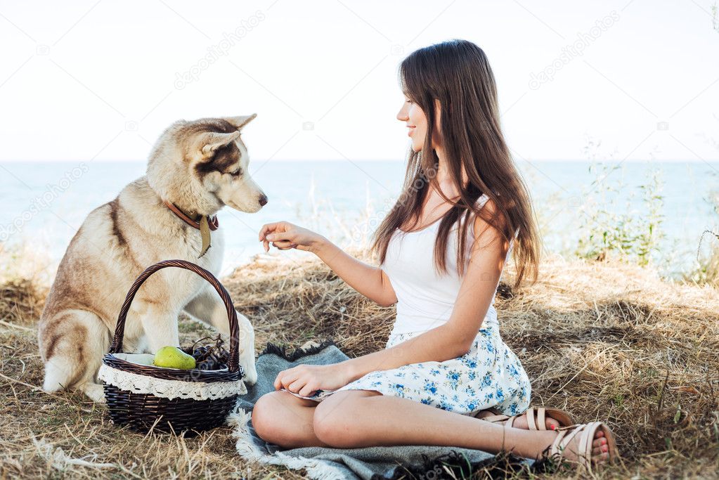 young caucasian female and red siberian husky dog on seaside with basket with fruits. eating fruits, healthy eating and healthy living concept
