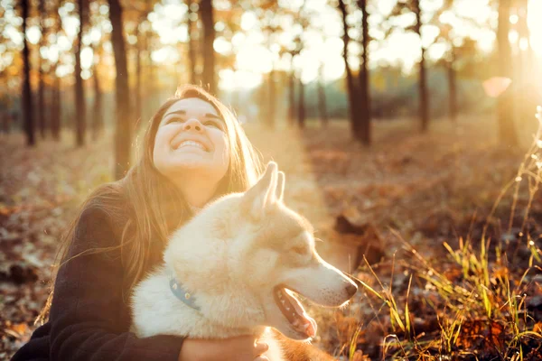 Jonge gelukkig vrouw plezier met Siberische husky hond in herfst park tijdens zonsondergang — Stockfoto
