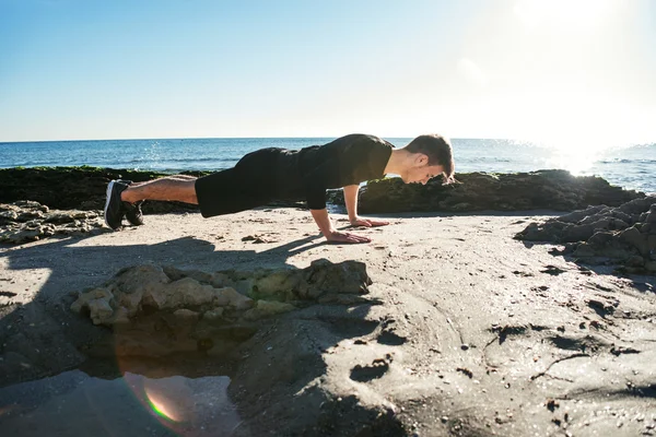 Junger Mann trainiert am Strand, sportlicher Mann macht Übungen — Stockfoto