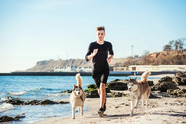 Laufmann. Läufer joggt mit sibirischen Huskyhunden während des Sonnenaufgangs am Strand — Stockfoto