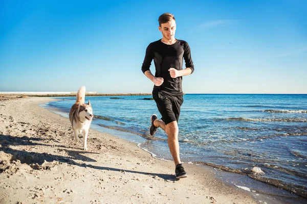 Kolejny człowiek. Mężczyzna runner jogging z psami husky syberyjski podczas słońca na plaży — Zdjęcie stockowe