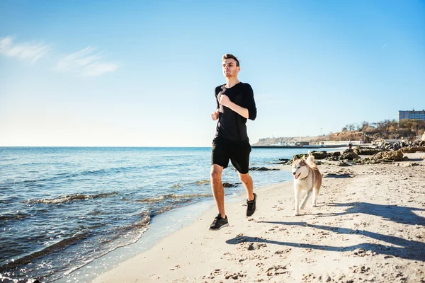 Laufmann. Läufer joggt mit sibirischen Huskyhunden während des Sonnenaufgangs am Strand — Stockfoto
