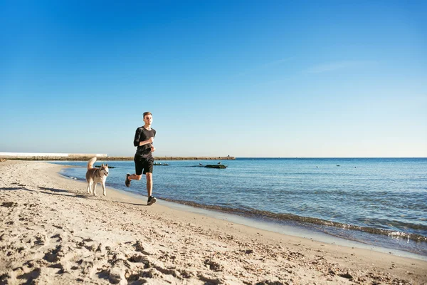 Běžící muž. Mužské běžce běhat s sibiřský husky psy během východu slunce na pláži — Stock fotografie