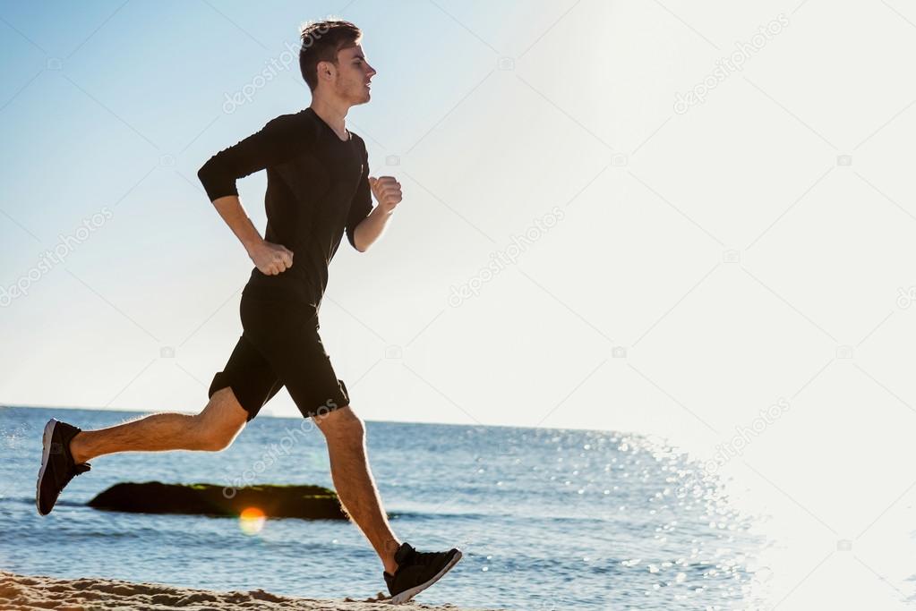 Running man. Male runner jogging during the sunrise on beach