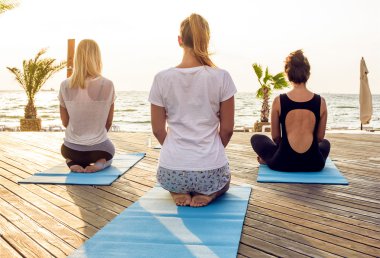 Grup genç kadın gündoğumu sırasında pratik yoga sahilde