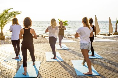 Grup genç kadın gündoğumu sırasında pratik yoga sahilde