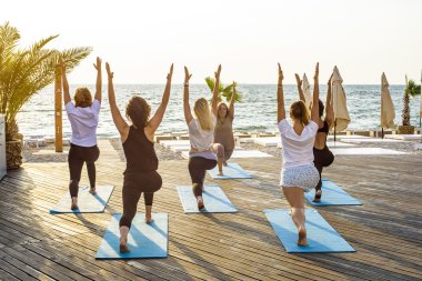 Grup genç kadın gündoğumu sırasında pratik yoga sahilde