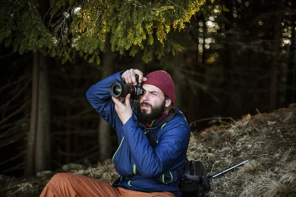 Jovem barbudo macho com câmera na madeira, fotógrafo tirar fotos em montanhas — Fotografia de Stock