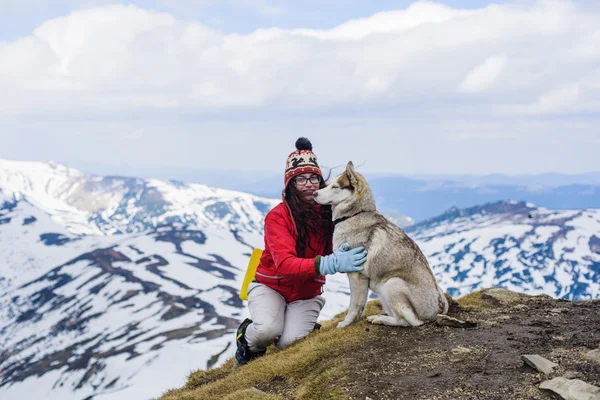 Girl sitting with sled dog in mountains — Stock Photo, Image