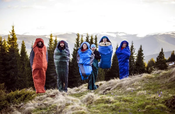 Cheering group of hikers jumping in sleeping bags outdoors in mountains during the sunset — Stock Photo, Image