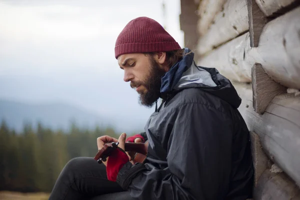 Cara barbudo jogando ukulele em montanhas perto de casa de madeira — Fotografia de Stock