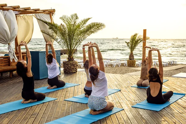 Grup genç kadın gündoğumu sırasında pratik yoga sahilde