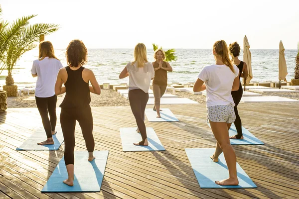 Grupa młodych samic praktykowania jogi na plaży podczas sunrise — Zdjęcie stockowe