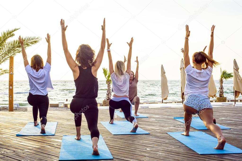 group of young females practicing yoga on the seaside during the sunrise