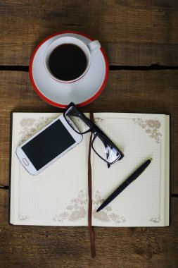 kahve fincanı, not defteri, cep telefonu, gözlük ve ahşap zemin üzerine kalem
