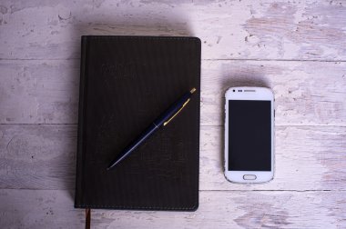Not Defteri, cep telefonu ve beyaz vintage ahşap zemin üzerinde kalem