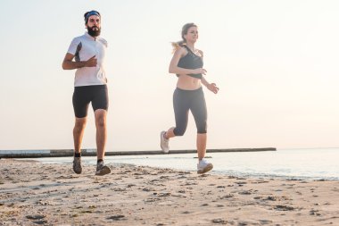 Kişi - kadın ve erkek atlet koşucular sahilde koşu çalışmıyor. Sağlıklı yaşam tarzı açık havada gündoğumu veya günbatımı sırasında egzersiz genç fitness çift uygun