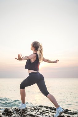 Fitness spor modeli mutlu gülümseyerek gündoğumu açık çalışma sırasında egzersizleri yapıyor. Güzel beyaz kadın eğitim dışında sahil sabah
