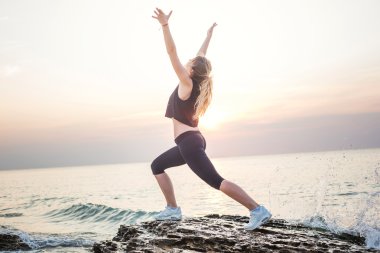 Fitness spor modeli mutlu gülümseyerek gündoğumu açık çalışma sırasında egzersizleri yapıyor. Güzel beyaz kadın eğitim dışında sahil sabah