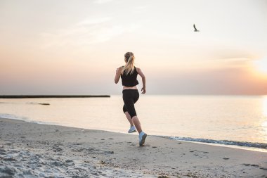 Çalışan kadın. Kadın atlet gündoğumu sırasında sahilde koşu.