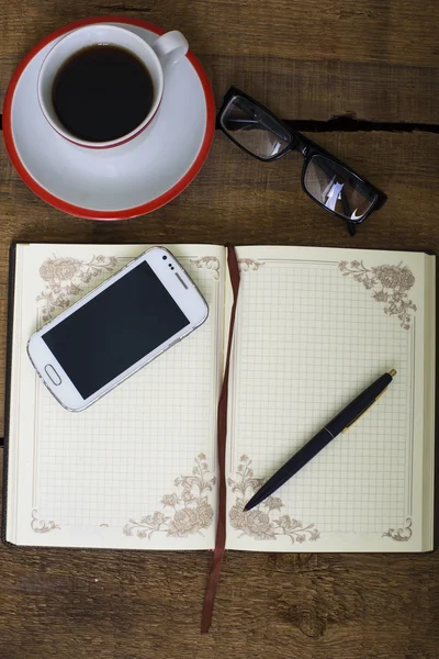 コーヒー カップ、メモ帳、携帯電話、メガネ、ペンが木製の背景に — ストック写真