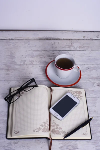 カップ、メモ帳、携帯電話、メガネ、ペンを白のヴィンテージの木製の背景に — ストック写真