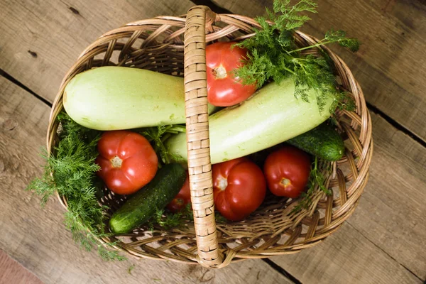 Fresh vegetables, cucumbers, squash, tomatoes and fennel in a wicker basket on wooden background — Stock Photo, Image