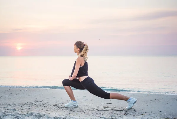 Modello di sport fitness sorridente felice facendo esercizi durante il lavoro all'aperto all'alba. Bella formazione femminile caucasica al di fuori sul mare al mattino — Foto Stock