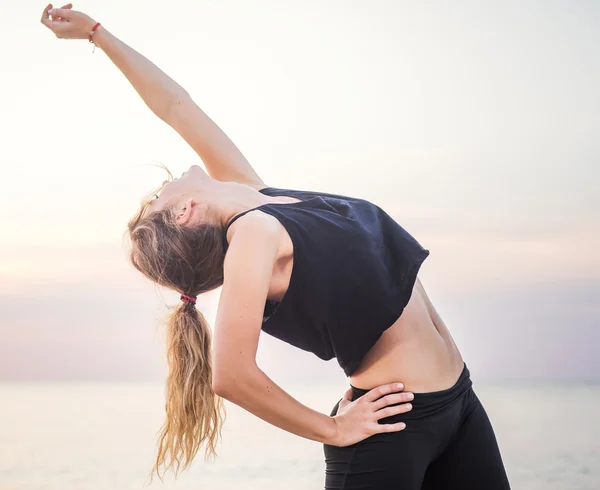 Modello di sport fitness sorridente felice facendo esercizi durante il lavoro all'aperto all'alba. Bella formazione femminile caucasica al di fuori sul mare al mattino — Foto Stock