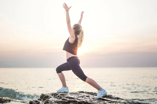 Fitness modelo deportivo sonriendo feliz haciendo ejercicios durante el ejercicio al aire libre a la salida del sol. Hermosa mujer caucásica entrenamiento al aire libre en la playa por la mañana —  Fotos de Stock